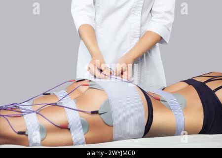 There is a woman, who is lying and is making anti cellulite procedure of myostimulation  on the legs and buttocks in a beauty salon. Caring for the bo Stock Photo
