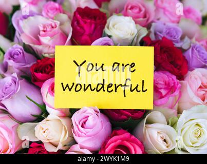 A yellow greeting card with words You are Wonderful laying on a big bouquet of colorful roses Stock Photo