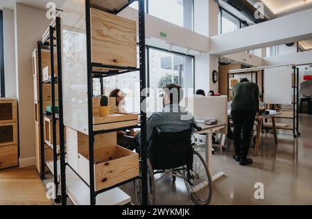 Diverse office setting featuring a wheelchair user working with colleagues in a contemporary workspace, promoting inclusivity and accessibility. Stock Photo