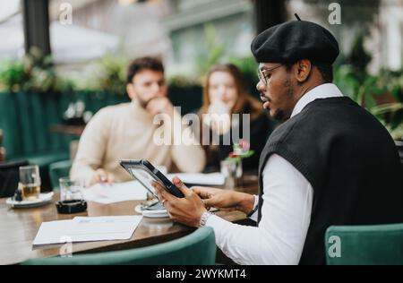 Stylish businessman using tablet at outdoor cafe meeting with colleagues. Stock Photo