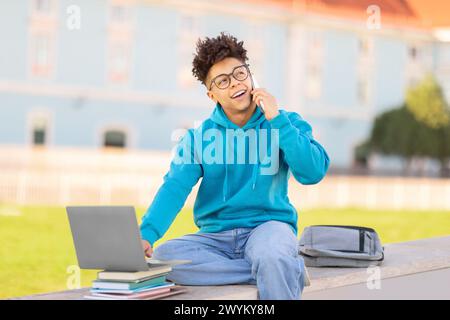 Student talking on phone with laptop, studying at park Stock Photo
