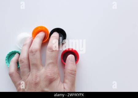 Woman's hand over five colorful plastic lids on white background, space for copy. Sustainability, recycling concept for June 5th World Environment Day Stock Photo
