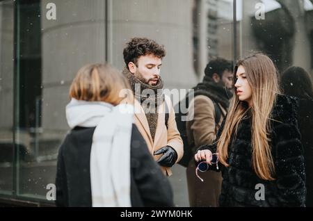A group of young business colleagues are engaged in a conversation outdoors with snowflakes around, projecting teamwork and discussion in winter. Stock Photo