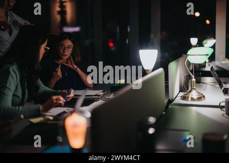 Two concentrated female business colleagues engaged in work during a late-night meeting in an office environment, showcasing teamwork and dedication. Stock Photo