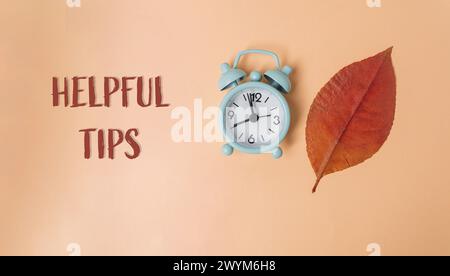 A clock with the hands on the numbers 12 and 6. The leaf is orange. The words Helpful Tips are written below the clock Stock Photo