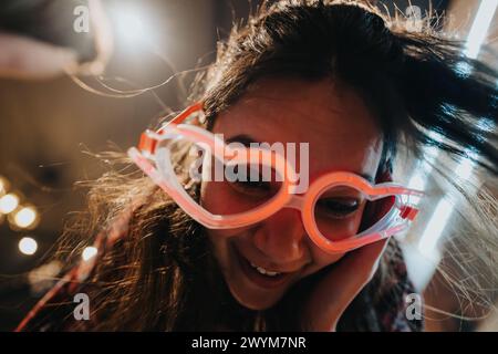 Joyful young woman with funky glasses laughing at a cozy home gathering Stock Photo