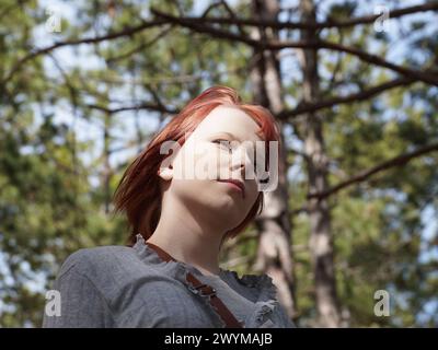portrait of a red-haired teenage girl in the forest, bottom view. Stock Photo