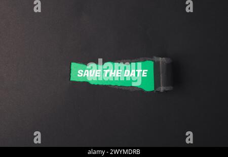 A torn piece of paper with the words save the date written on it. The paper is green and has a hole in it Stock Photo