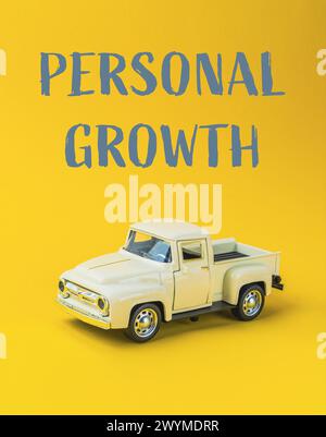 A toy truck is on a yellow background with the words Personal Growth written below it. Concept of personal growth and development, as the toy truck re Stock Photo