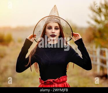 halloween portrait of teenage girl in witch hat smiling at camera on nature background Stock Photo