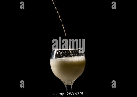 Fillet of milk with drops falling from above into a glass wine glass. Isolated on black background. Stock Photo