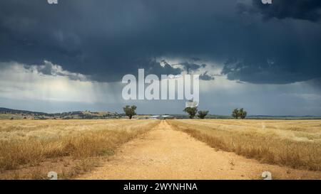 Looking down a country road through a dry field with rain falling from dark clouds above at Joyces Creek in Central Victoria, Australia Stock Photo