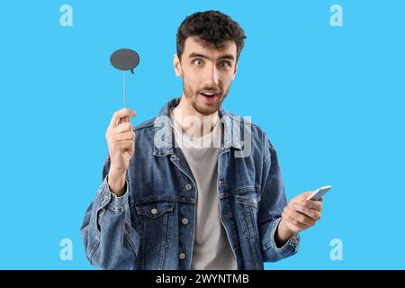 Surprised young man with speech bubble using mobile phone on blue background Stock Photo