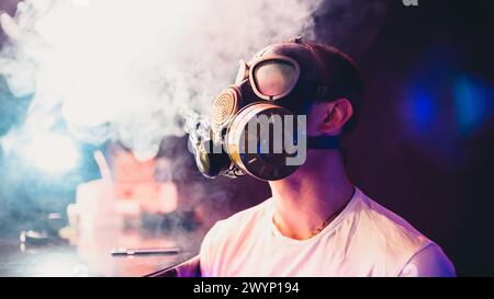 man in a gas mask Smoking a hookah and blowing smoke. Soft focus and small grain Stock Photo