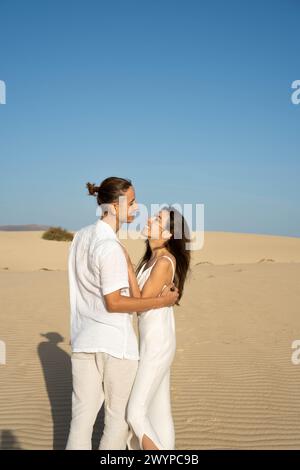Vertical view of young couple in white outfit looking to each other in sand dunes at the beach with clear sky in summer time Stock Photo