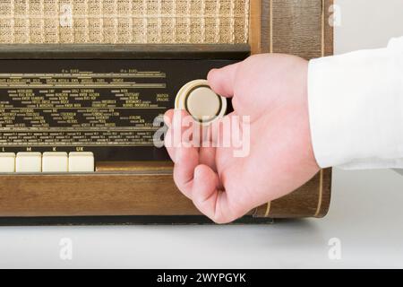 Authentic 60s radio receiver. Front view. On white background. Traces of time. A man's hand on the wave setting radio knob. Close-up Stock Photo