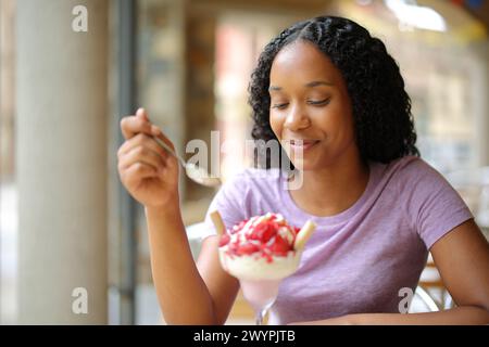 Black woman eating strawberry in a restaurant terrace Stock Photo