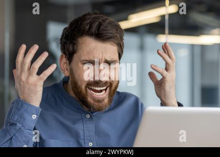 Adult male in a blue shirt feeling stressed and annoyed while facing computer issues in a modern office environment. Stock Photo