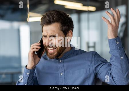 Frustrated male executive having a heated conversation on a smartphone in a modern office environment. Stock Photo