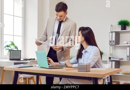 Two company employees sitting with laptop computer in office looking through financial documents. Stock Photo