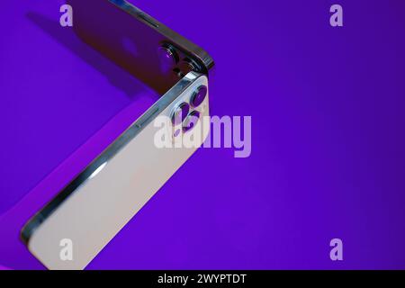 Paris, France - Sep 29, 2022: Close-up of two smartphones highlighting their advanced Apple Computers iPhones triple-lens cameras, set against a vivid orange background Stock Photo
