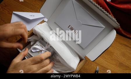 Paris, France - Jun 5th, 2020: Hands delicately unbox a luxury item from Dior, showcasing the elegant packaging and anticipation of revealing a high-end product Stock Photo