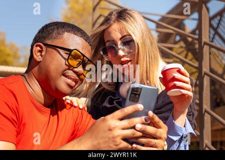 Happy interracial couple checking cell phone outdoors. Stock Photo