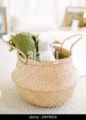 Light wicker basket with rolled blankets in a neutral space Stock Photo