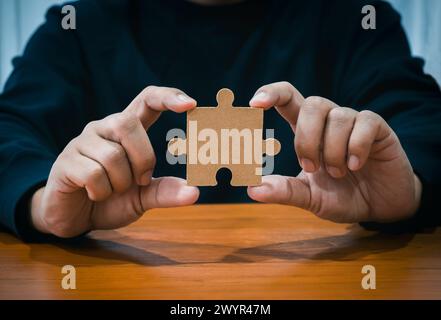 A jigsaw puzzle holding businessman's hand. Person hands showing empty piece of important jigsaw puzzle on wood table. Business solution and idea, par Stock Photo