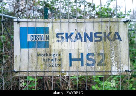 Harefield, UK. 8th April, 2024. A Costain Skanska HS2 sign on the fence of an HS2 construction site in Harefield near where water runs across a country road in Harefield. HS2 have dug up fields, felled numerous trees and destroyed hedges in the area. Waterways across where HS2 are working are having to find new routes which locals believe is exacerbating flooding issues across West London and the Chilterns. Credit: Maureen McLean/Alamy Live News Stock Photo