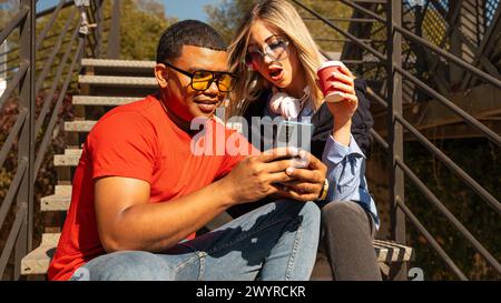 Happy interracial couple checking cell phone outdoors. Stock Photo