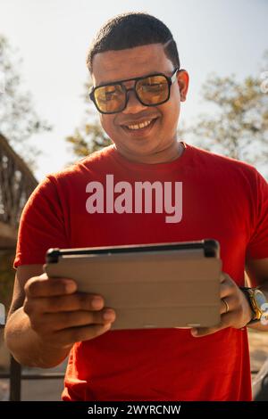 Vertical portrait glamorous smiling young man, sitting using a app on a digital tablet outdoors. Stock Photo