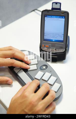 Person labeling a music CD using the braille BlueType keyboard The person writes the information using the braille bluetooth BlueType keyboard Later, this information will be transferred to the music CD bring the PDA equipped with the SD/NFC card closer to the tag placed on the CD, Home lab for testing and research trials for patients at home, Unit of Health Technology, Tecnalia Research & Innovation, Bizkaia Technology Park, Zamudio, Basque Country, Spain. Stock Photo