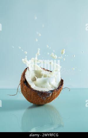 Cracked coconut and splashes of coconut milk on a blue background. Summer background. Stock Photo