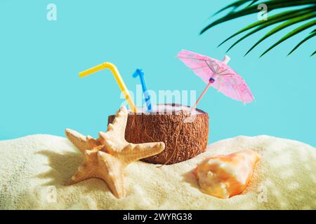Coconut with a straw, shells, starfish and a sun umbrella on the sand. Summer background, concept of relaxation and vacation. Stock Photo