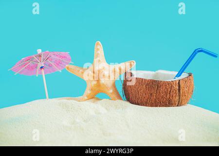 Coconut with a straw, shells, starfish and a sun umbrella on the sand. Summer background, concept of relaxation and vacation. Stock Photo