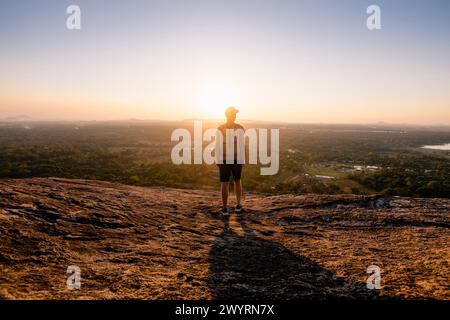 Rear view of man with backpack on rock overlooking sunset over tropical landscape. Travel in Sri Lanka. Stock Photo