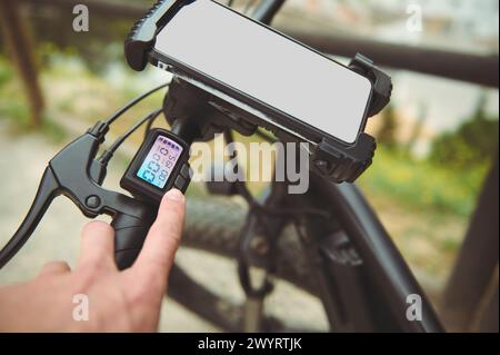 Close-up cyclist adjusting program on digital screen while riding electric bike outdoors. Fixed smart phone with mockup screen. Copy ad space for mobi Stock Photo