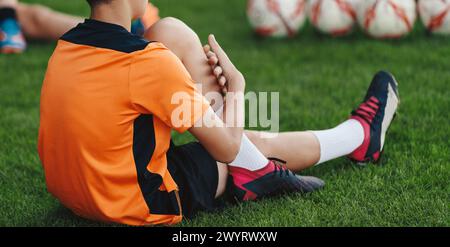 Young Boys in Sports Uniform Sitting and Stretching on Grass Field. Kids in Soccer Club on Training Unit. Kids Play Team Sports. Boy Pulling Knee To C Stock Photo