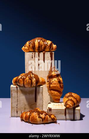 Chocolate-covered croissant in a styled pyramid display of wooden blocks on blue background Stock Photo