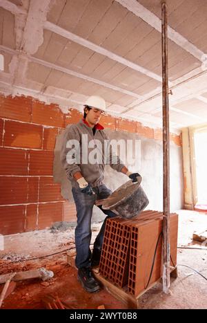 Bricklayer with trowel, bricks, new homes under construction, construction site. Stock Photo