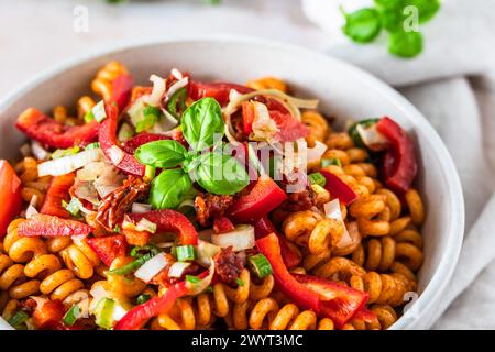 Pasta salad with red pepper, tomatoes, spring onions and basil in a white bowl on light background Stock Photo