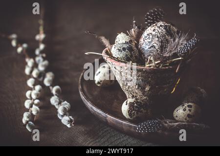 Easter decoration: rustic flower pot with natural quail eggs and feathers on a dark wooden plate and table Stock Photo