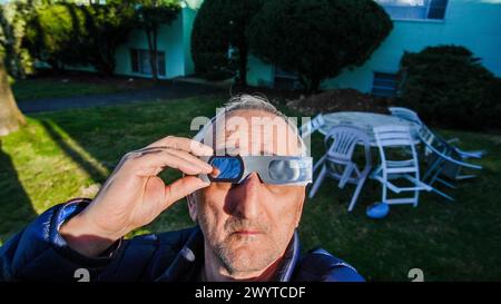 NORWALK, CT, USA - APRIL 8, 2024: Senior man with protective American Eclipse  glasses looking up to sky Stock Photo