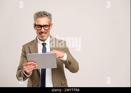 Seasoned businessman with grey hair and glasses confidently using a tablet, his smile suggesting ease with technology that bridges the gap between traditional business acumen and modern digital trends Stock Photo