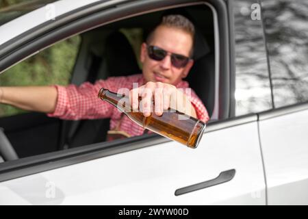 Bavaria, Germany - April 7, 2024: Man in traditional Bavarian costume celebrates drunk with a bottle of beer in a car. Symbol photo drunk and intoxicated driving *** Mann in bayerischer Tracht feiert betrunken mit einer Flasche Bier in einem Auto. Symbolfoto alkoholisiert und betrunken Autofahren Stock Photo