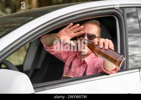 Bavaria, Germany - April 7, 2024: Man in traditional Bavarian costume celebrates drunk with a bottle of beer in a car. Symbol photo drunk and intoxicated driving *** Mann in bayerischer Tracht feiert betrunken mit einer Flasche Bier in einem Auto. Symbolfoto alkoholisiert und betrunken Autofahren Stock Photo