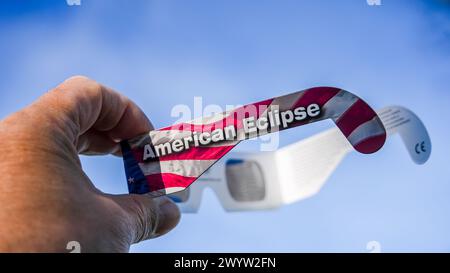 NORWALK, CT, USA - APRIL 8, 2024: A hand is shown holding a eclipse glasses with American Eclipse printed on them, adorned with the United States flag Stock Photo