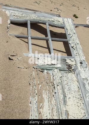 Broken door with peeling, white paint, lying in the sand in Bogenfels abandoned mining village. Stock Photo