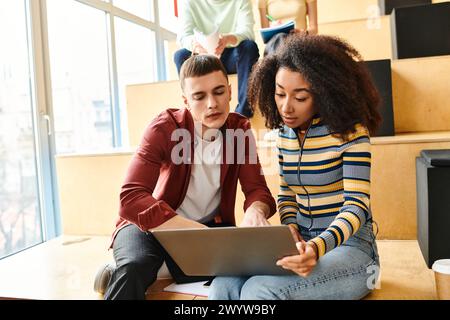 A black girl and a man sit on the floor, focused on a laptop screen, engaged in collaborative learning Stock Photo